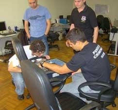 Policiais periciam computador apreendido: aplicativo pode ter sido usado para desviar milhes