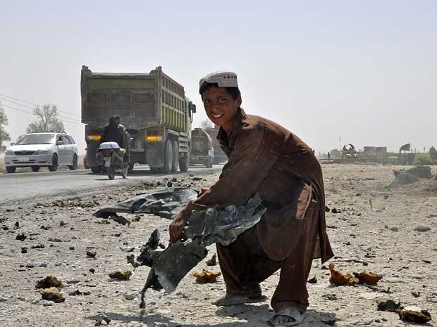 Crian�a afeg� levanta um destro�o de um ve�culo no local de um ataque suicida em Kandahar.