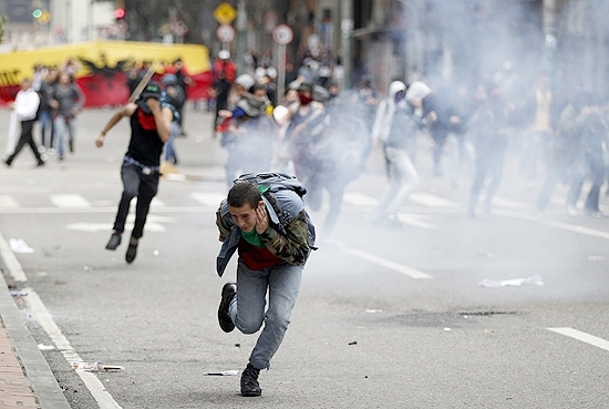 Manifestante corre para escapar de gs lacrimogneo durante protesto nas ruas de Bogot