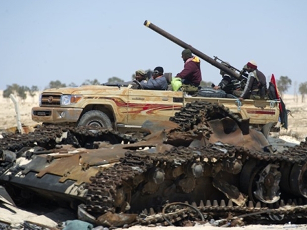 Rebeldes passam por tanque destrudo das tropas de Kadhafi neste domingo (10) em Ajdabiyah